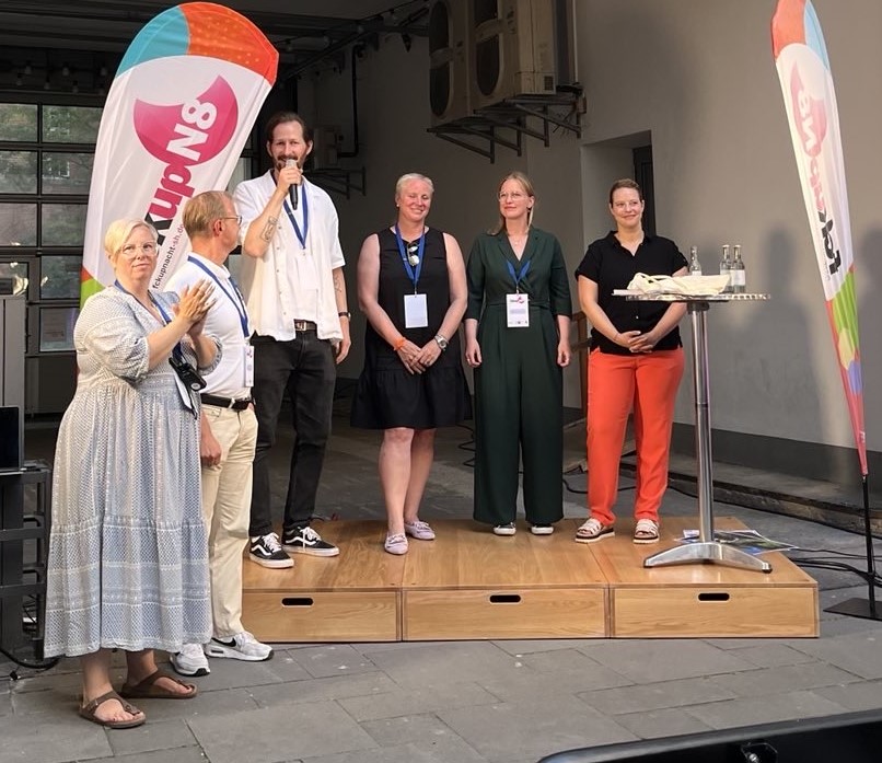 Sechs Personen auf einer kleinen Bühne bei einer Live-Veranstaltung open air.