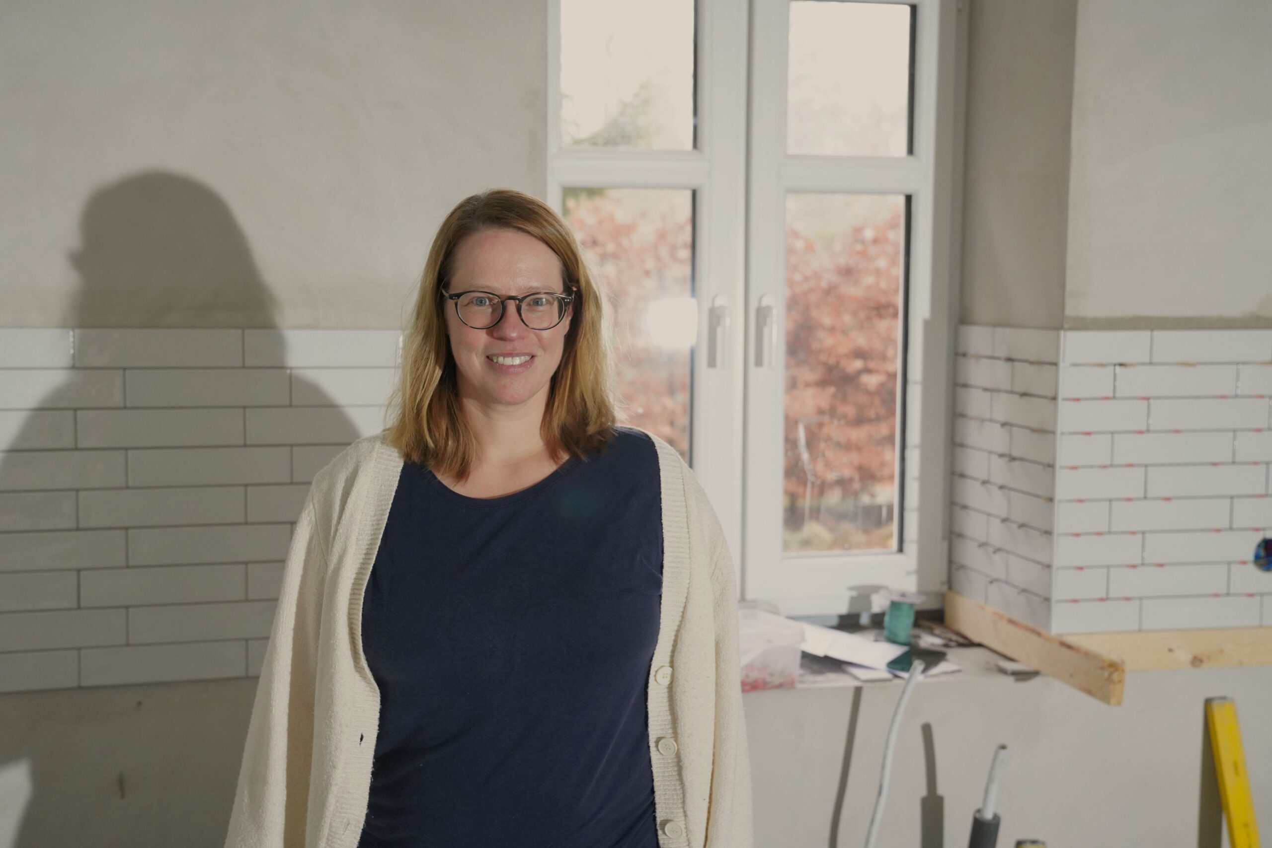 Die Bauherrin Sonja steht vor dem Fliesenspiegel in der zukünftigen Küche und ist sichtlich zufrieden